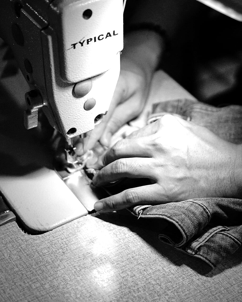 Hands guiding denim through a sewing machine